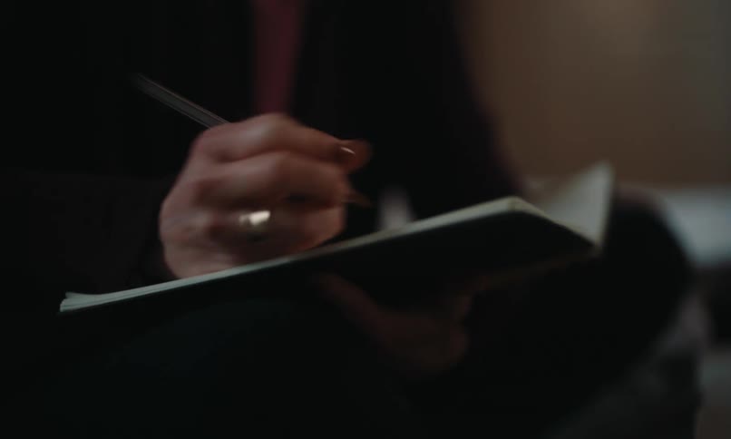 A woman smiles as she writes in her notebook and uses a computer