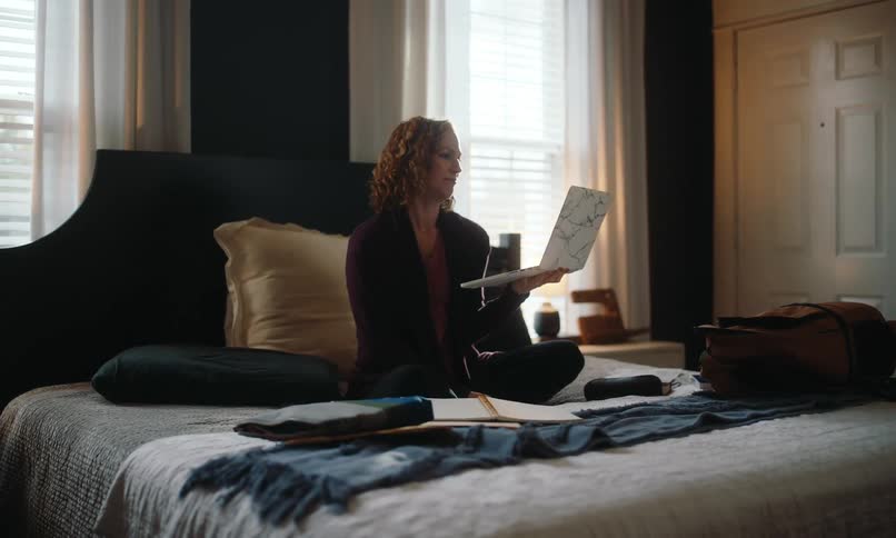 Woman sitting on her bed on an autumn day holds her laptop up during a video meeting