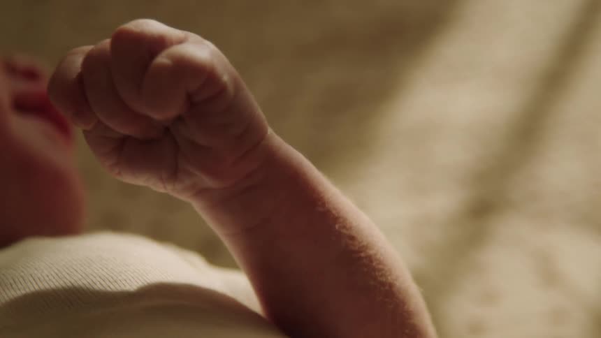 A baby clinches his fist in the crib