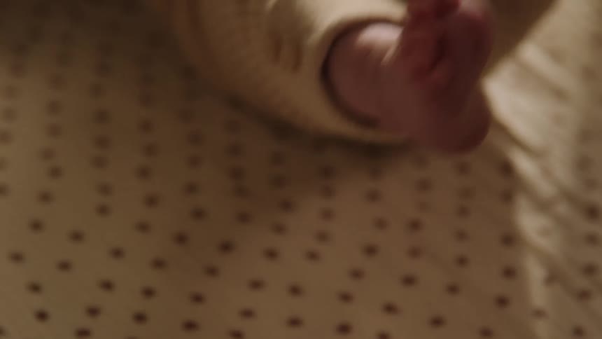 A closeup of a babys foot in a beige onesie resting on a patterned fabric