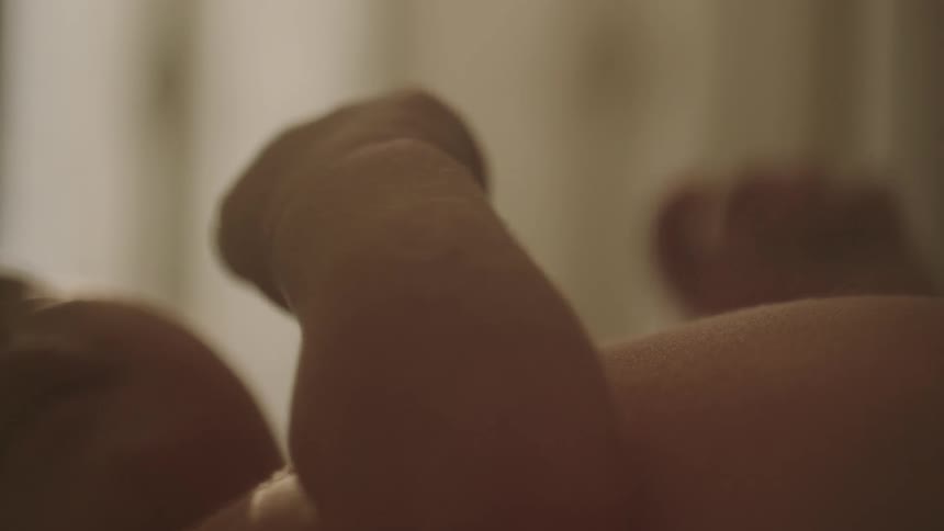 Closeup of a bare chested baby resting on a bed with their arms shaking