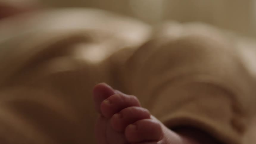 A closeup of a babys foot in a beige onesie resting on a bed