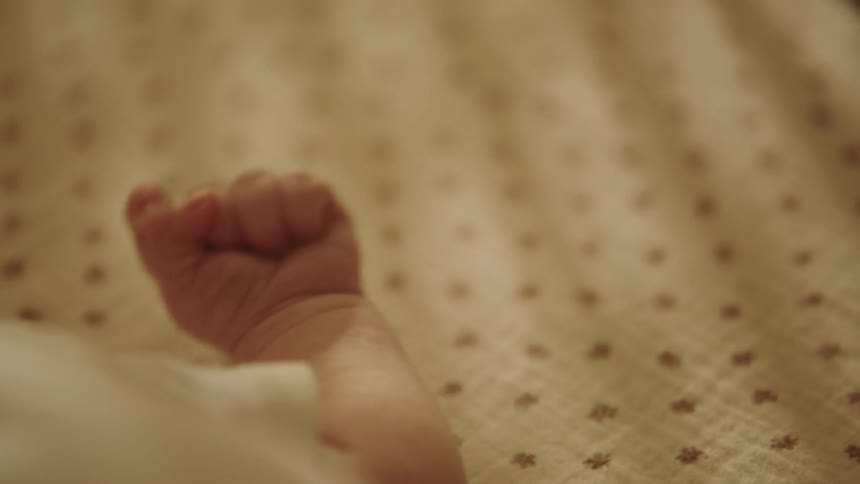 A closeup of a babys hand resting on a patterned blanket