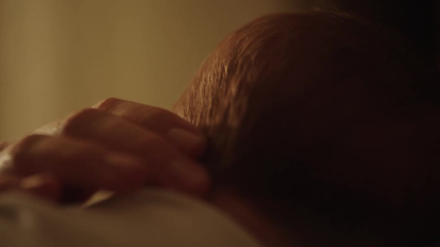 A person is holding a baby in a warmly lit room gently caressing the back of the babys neck