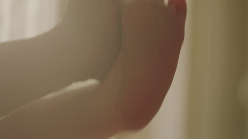 Two tiny baby feet wave playfully in the air their soft skin illuminated against a blurry sunlit background