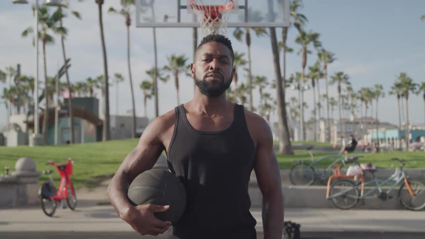Man holding a basketball poses while standing on the basketball court in the park on a sunny summer day
