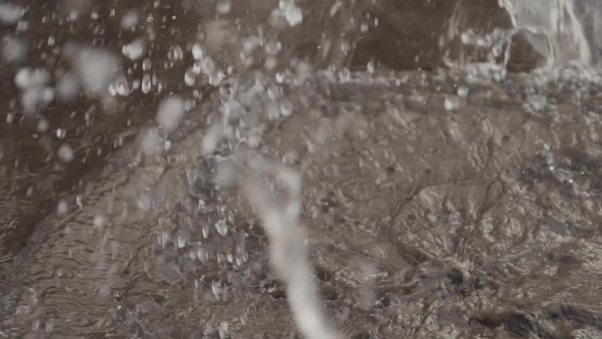 A brown boot with yellow laces is splashing through a puddle creating a dynamic spray of water
