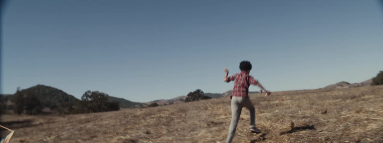 Boy running through a field playing with a kite