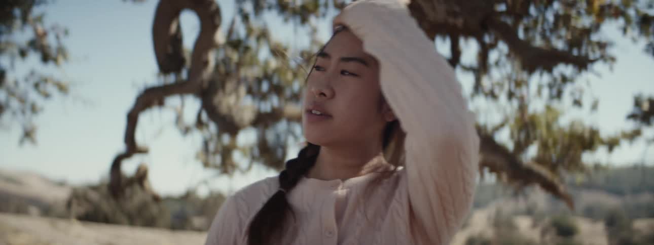 Woman placing her hand on her head while standing in a natural location surrounded by trees