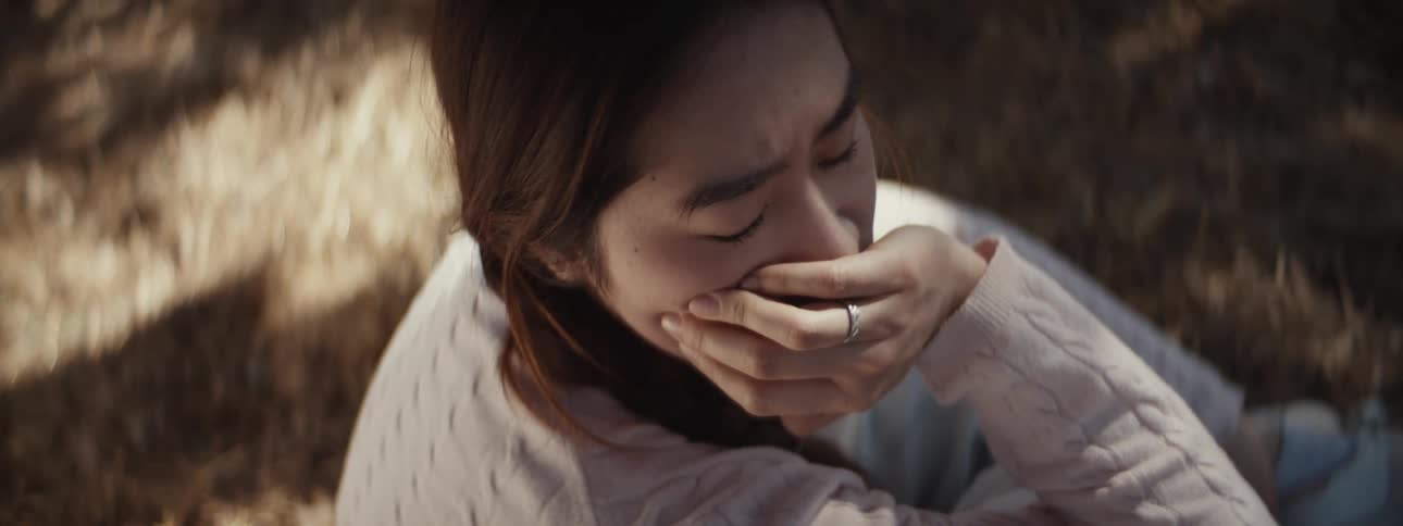 A woman holds her face while sitting on the grass