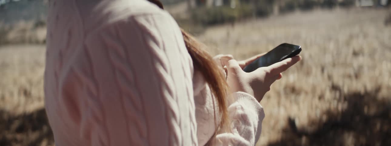 Woman in a field outdoors interacting with a smartphone