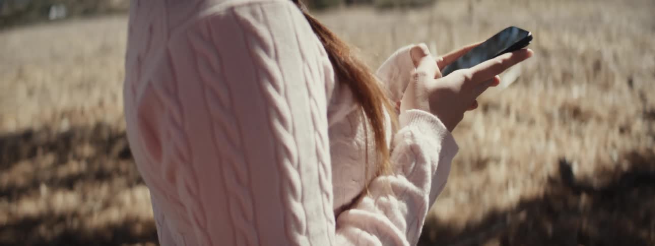 A woman is texting on her cell phone standing on the grass