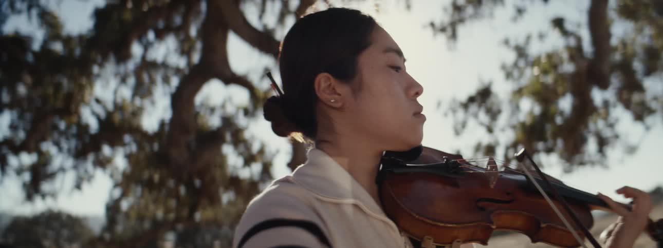 A woman is playing the violin under the tree branches