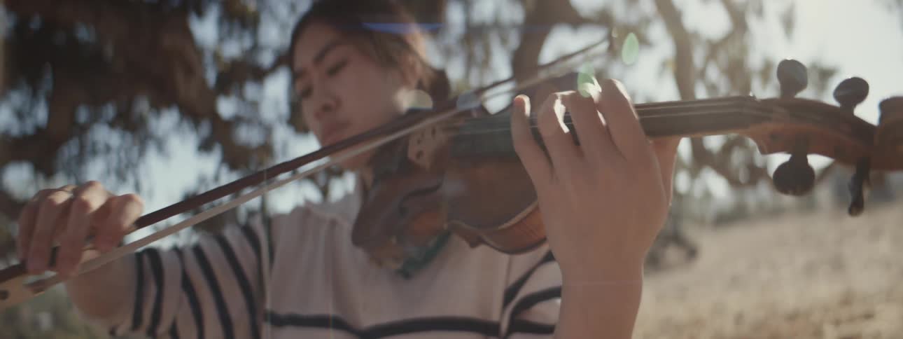 Woman playing violin outdoors under a tree