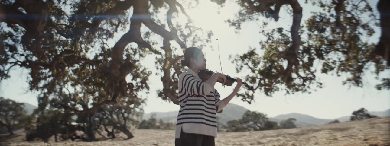 A woman is playing the violin under the bright sun