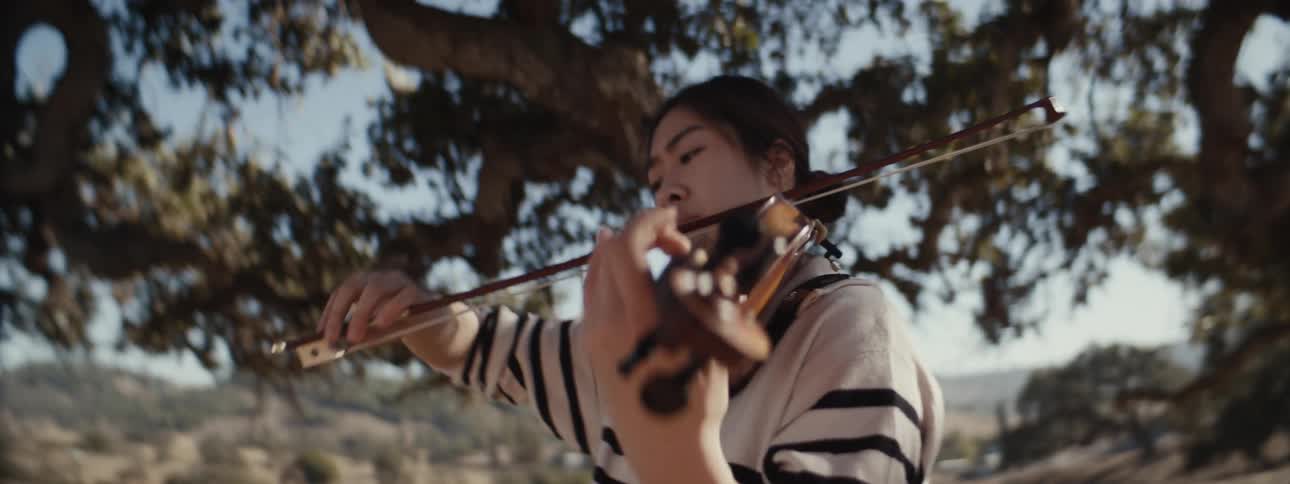 A woman is playing the violin in the shade of a tree