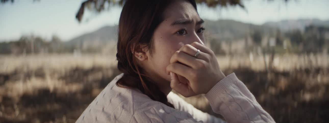 Side portrait of a young woman crouching with a worried expression while standing in a field