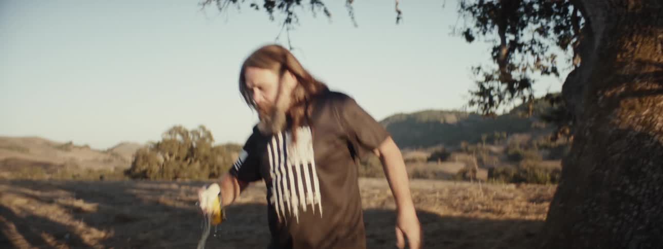 Man climbing down from a tree with a can of beer and drinking it