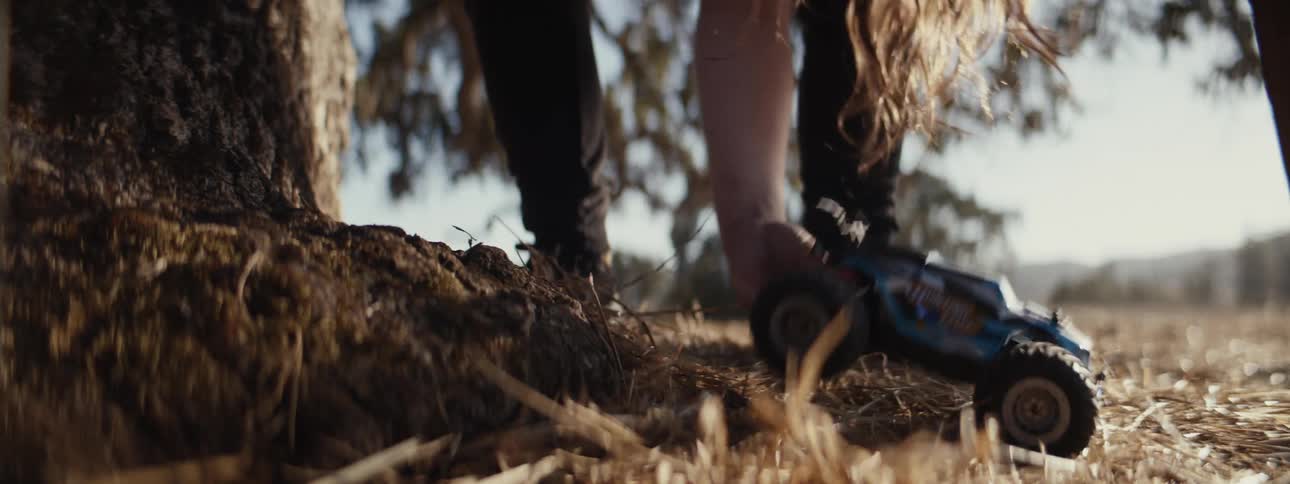 A girl runs through a grassland to pick up her remotecontrolled toy car