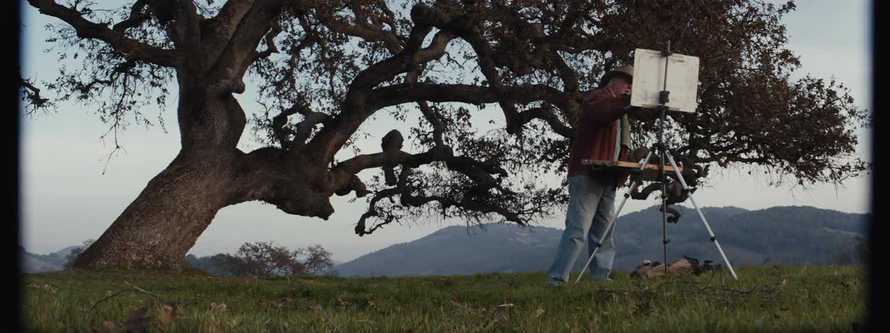 Man painting a picture next to a tree in a natural setting