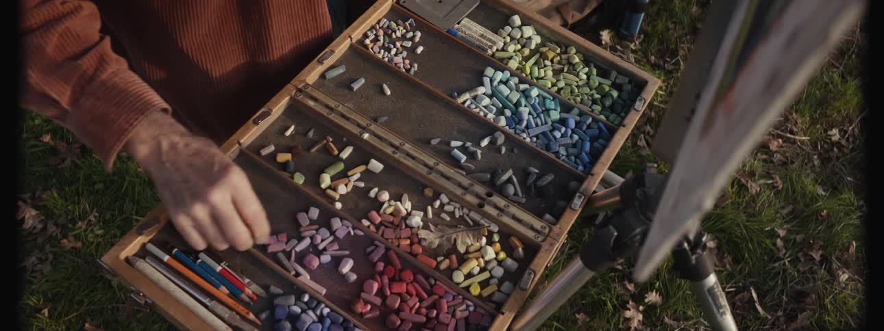 Illustrators arm taking different colored chalk and painting a picture