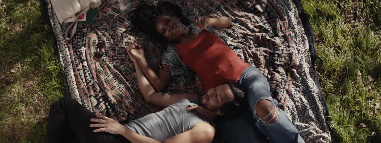 A young pregnant couple lies on a blanket spread over green grass