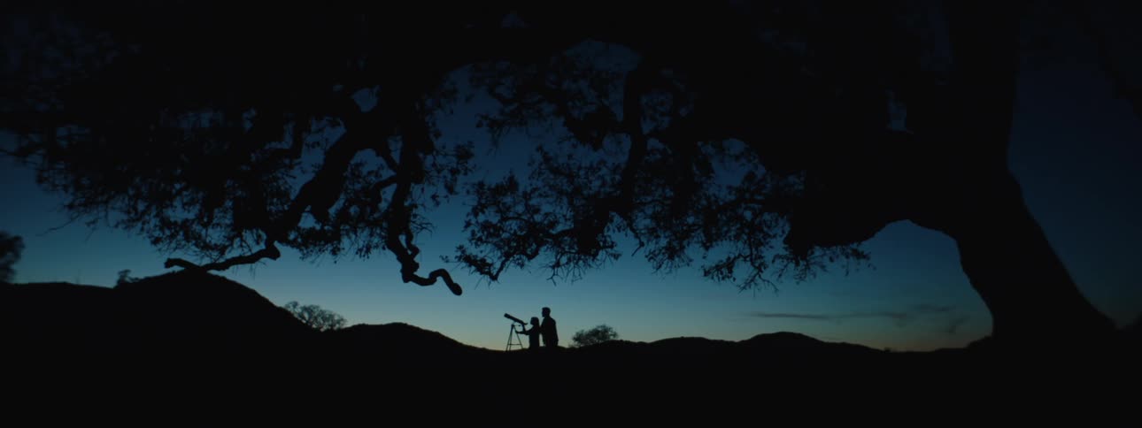 Silhouettes of two people watching the night sky with a telescope