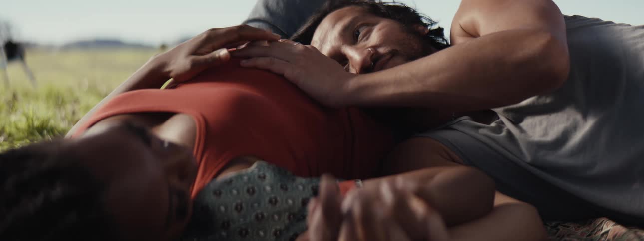 Couple lying on the grass while the man places his hand on the pregnant womans belly
