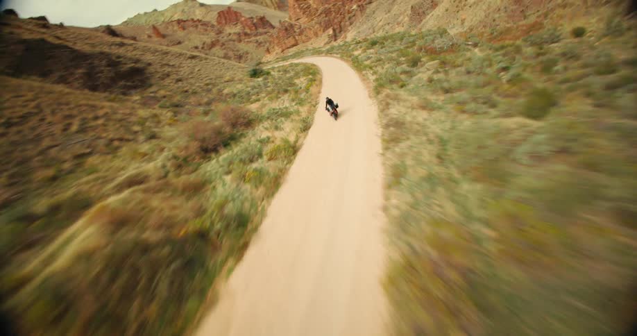 Aerial view of a motorcycle traveling along a narrow dirt road surrounded by canyons