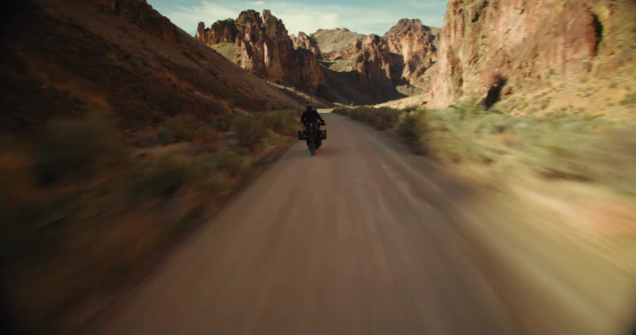 Aerial view of a person riding a motorcycle on a narrow road surrounded by mountains