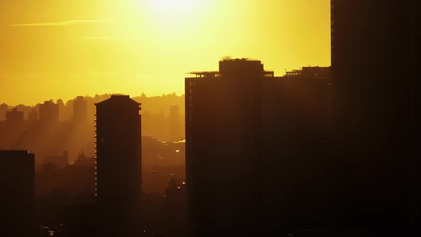 Aerial panorama of a skyline of a metropolis silhouette with the golden sun on the horizon