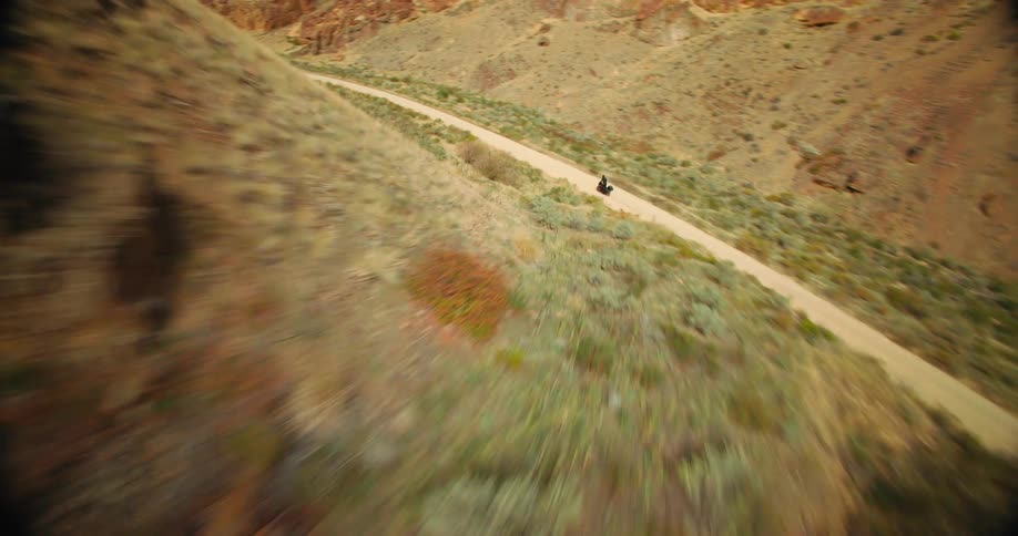 Aerial view of a motorcycle traveling along a narrow dirt road surrounded by mountains