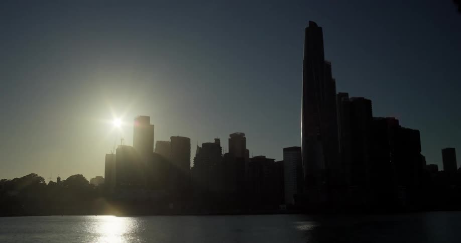 The silhouette of a city facing the sea with the sun in the sky and it getting dark