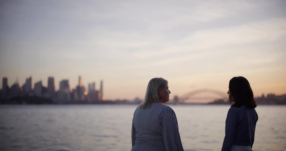 Two women talking by the sea and a city in the background