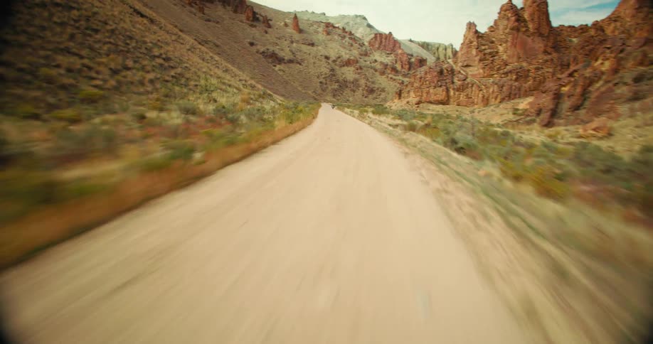 Aerial view of a person riding a motorcycle on a narrow road surrounded by barren mountains