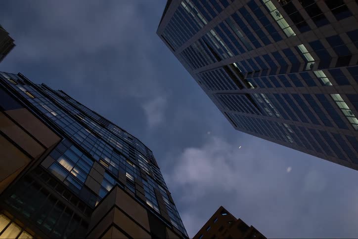 Looking up at two towering skyscrapers from a low angle the shot captures their geometric forms against a darkening sky