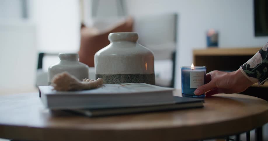 Hand placing a lit scented candle on top of a wooden table in a living room