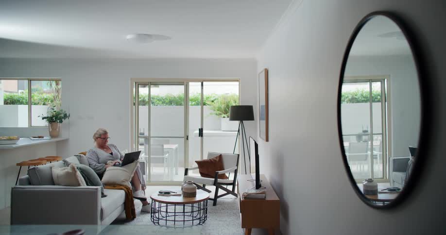 A modern living room with a person sitting on a couch using a laptop