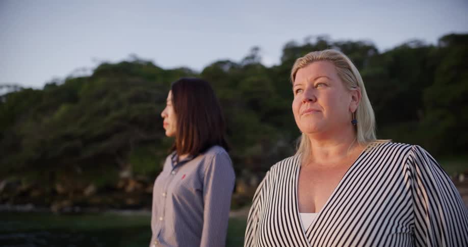 Two women standing side by side on a coastal landscape gazing at the sky