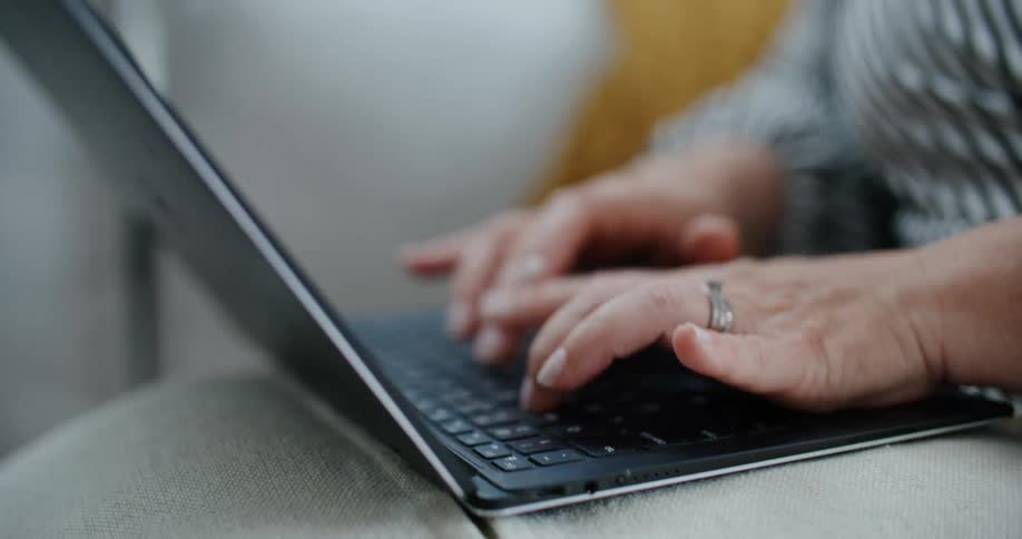 An older womans hands typing on a laptop keyboard