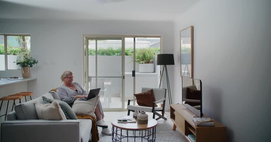 A woman is typing on her laptop in her living room