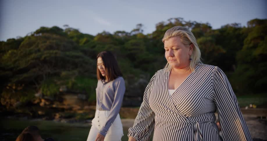 Two women walking in a natural area with the wooded coastline in the background