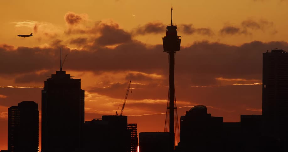 A commercial airplane flies over a metropolis at sunset