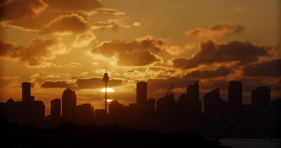 An airplane flies over a city with buildings shown in silhouette form