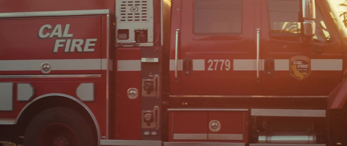 Sun shines from a red tinted sky onto a cal fire truck parked near burnt debris