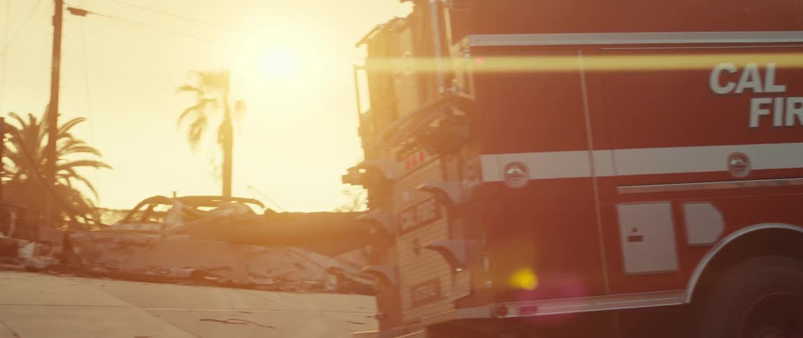 Firetruck sits parked near burnt debris under a red tinted sky