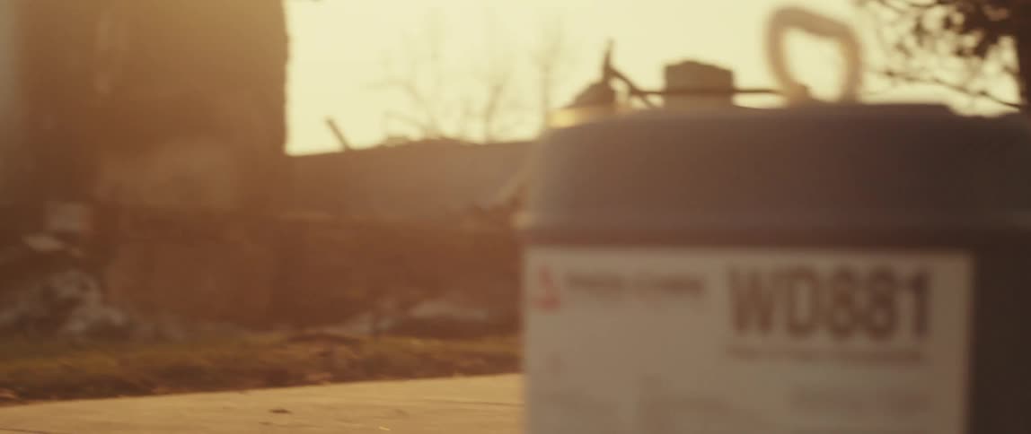 Sun shines onto a firefighting chemical container sitting on the ground across the street from a burnt building