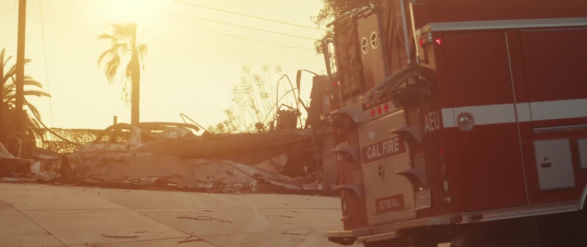 A red fire truck in front of some concrete debris on a day with strong orange sunlight in the background