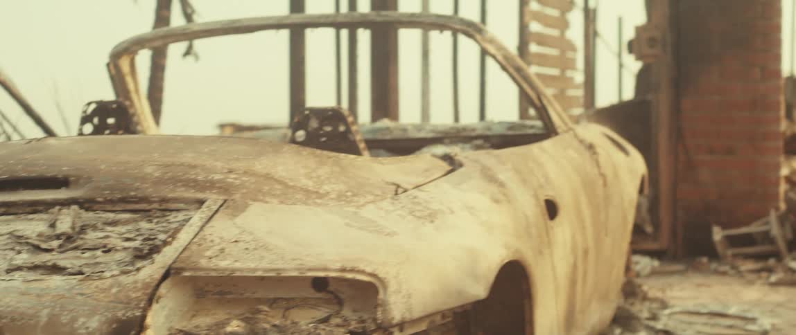 A wrecked car covered in dust next to a destroyed structure