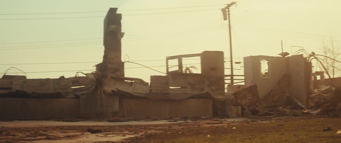 The skeletal remains of a burnedout structure stand against a hazy sky with debris scattered across the foreground